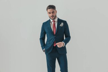 Stüdyoda, gri arka planda eli cebinde poz veren lacivert takımlı zarif bir adamın portresi.