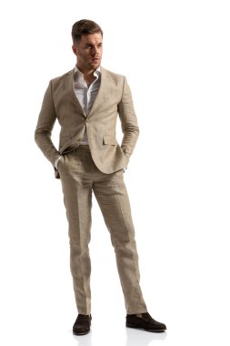 Uzun boylu, elleri ceplerinde yakışıklı bir adam stüdyo ortamında beyaz arka planda soyutlanmış bir şekilde poz veriyor.