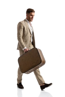 Takım elbiseli, açık yakalı, valizli, tatile çıkan, beyaz arka planda tek başına yürüyen ve stüdyoda poz veren seksi bir genç.