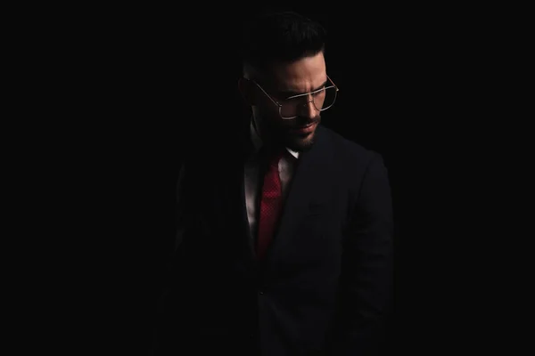 セクシーな若いビジネスマンの肖像画でエレガントなスーツとともに赤いネクタイ見下ろしとポージングで劇的な方法で黒の背景にスタジオ — ストック写真