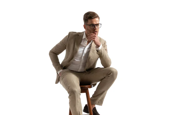性感小伙子 膝盖上有肘部 嘴唇敏感 手插在口袋里 坐在工作室的白色背景上 — 图库照片