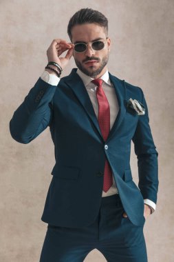 Bej arka planda el ele tutuşan havalı seksi adam güneş gözlüğünü ayarlıyor ve poz verirken kendine güveniyor.