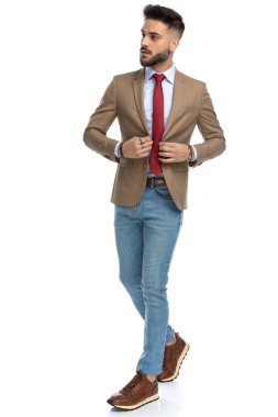 Stüdyoda beyaz arka planda tek başına yürürken ve yan tarafa bakarken seksi sakallı adamın ceketini kapatırken tüm vücudu.