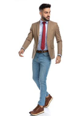 Stüdyoda beyaz arka planda, tüm vücudunu sarmış, yan tarafa bakan ve yürüyen kravatlı seksi, zeki ve rahat bir adam.