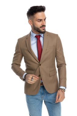 Kırmızı kravatlı sakallı genç adam beyaz arka planda poz veriyor.