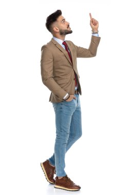 El ele tutuşmuş çekici bir adam, gökyüzüne bakıyor ve parmağıyla işaret ediyor, yürüyor ve beyaz arka planda poz veriyor.