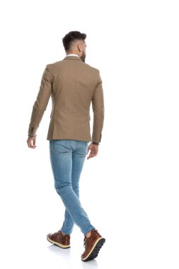 Stüdyoda beyaz arkaplan önünde poz veren sakallı genç bir adamın arkasında.