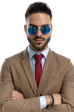 Beyaz arka planda rahatça poz verirken gözlük takan ve çapraz kollu şık iş adamı.