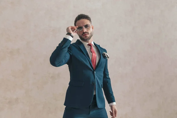 cool elegant guy wearing stylish outfit with handkerchief adjusting sunglasses in front of beige background, standing and posing in studio