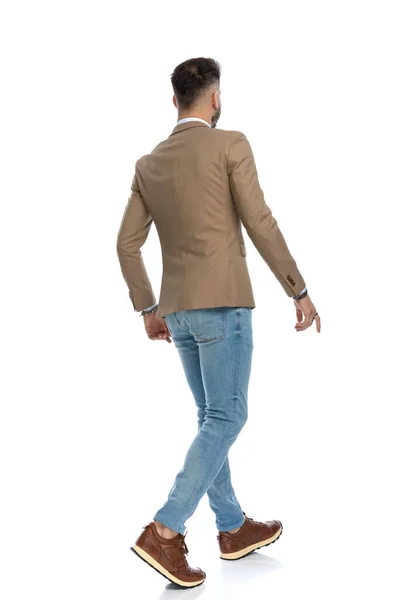 スマートなカジュアルなジャケットと青いジーンズを着た男が スタジオの白い背景の前で歩くとポーズをとって — ストック写真