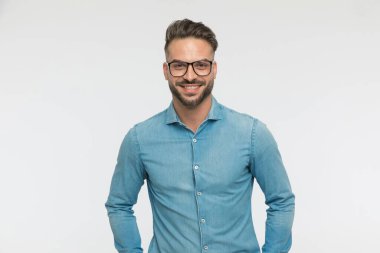 Gözlüklü, kameraya gülümseyen ve gri arka planda poz veren seksi bir adam.