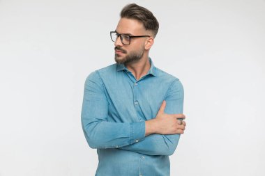 Yakışıklı adam havalı bir tavır sergiliyor, yana bakıyor ve gri arka planda gözlük takıyor.