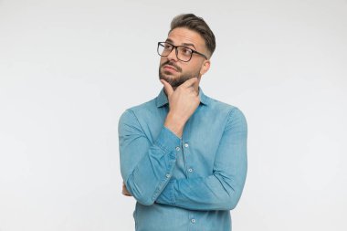 Genç, sıradan bir adam, gri stüdyo geçmişine karşı bir fikir düşünürken çenesini kaşıyor.