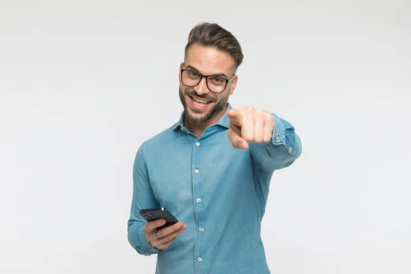 Привабливий Випадковий Чоловік Вказує Камеру Тримає Телефон Великою Посмішкою Сірому — стокове фото