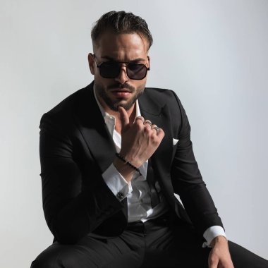 Zarif smokinli havalı sakallı bir adamın portresi. Üstü açık tişörtlü. Düşünceli ve gri arkaplandaki hayati kararları düşünen.