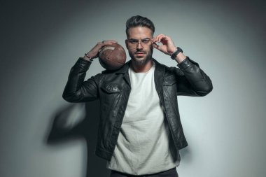 Yakışıklı, sıradan bir adam gözlüğünü takıyor ve omzunda bir rugby topu tutuyor. 