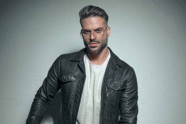 Çekici, sıradan bir adam yüzünde sert bir ifadeyle gri arka planda gözlük takıyor.