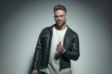 Şehvetli pozlar veren genç bir adam, siyah deri ceket ve gözlük takıyor. 