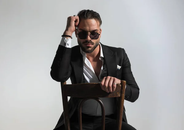 穿着黑色燕尾服 手肘握在旧木椅上 在灰色背景中以时尚的方式摆姿势的酷哥肖像 — 图库照片