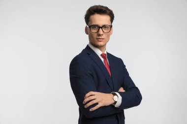 Şık takım elbise giyen, kollarını kavuşturan ve stüdyoda gri arka planda poz veren gururlu iş adamının portresi.