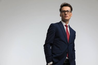 Elleri ceplerinde zarif genç bir işadamı. Stüdyoda gri arka planda poz veriyor.