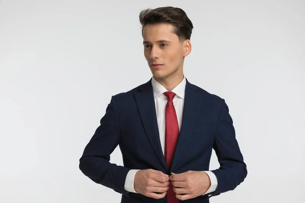 年轻的商人 戴着红色领带 系着海军蓝西服 在工作室里摆出灰色背景的姿势 朝旁边看去 — 图库照片