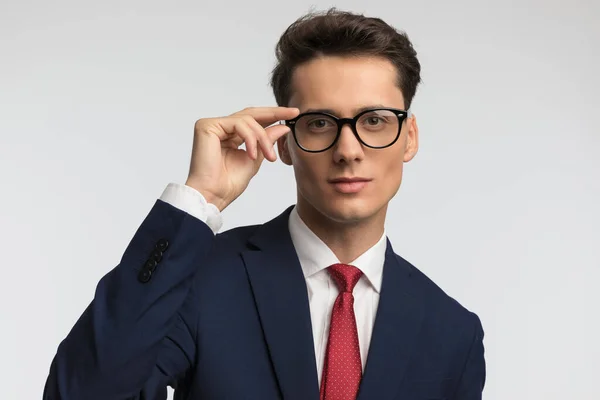 雅致的商人 戴着红色领带 微笑着 在工作室灰色背景前调整着眼镜 — 图库照片