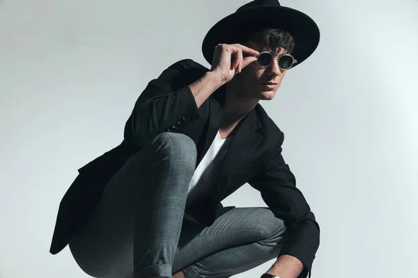 Sexy Young Man Black Hat Looking Side Fixing Sunglasses While — стоковое фото