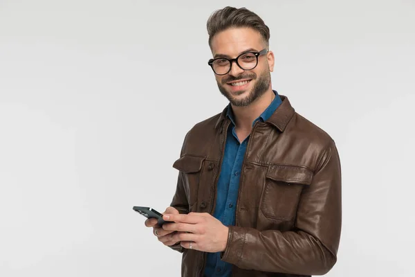 Joven Feliz Chaqueta Cuero Marrón Sosteniendo Teléfono Sonriendo Desplazándose Por —  Fotos de Stock