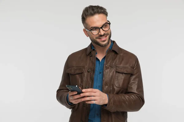 在工作室里 戴眼镜的快乐男人一边在社交媒体上翻来覆去 一边看着灰色背景的手机 — 图库照片
