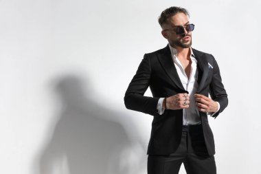 Seksi iş adamı smokinini ayarlıyor, başka bir yere bakıyor ve güneş gözlüğü takıyor.