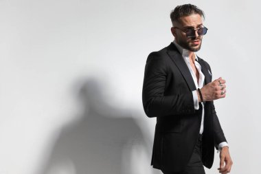 Havalı iş adamı seksi duruşu ve siyah smokin giymesi ve gri stüdyo arka planına karşı papyon takması.