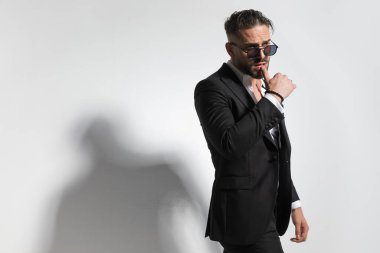 Çekici iş adamı, şehvetli, dudaklarına dokunan, siyah smokin giyen ve gri stüdyo arka planına yaslanmamış papyon takan.