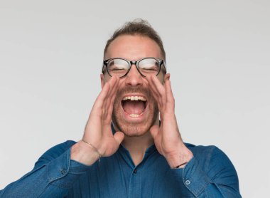 Genç adam tüm ciğerleriyle bağırıyor, gözlük takıyor ve mavi gömlek giyiyor.