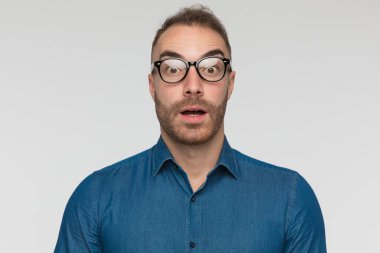 Genç adam tamamen şokta, gözlük takıyor ve mavi gömlek giyiyor.