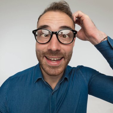 Deli adam biraz kafası karışık ve gri stüdyo arka planında mavi gömlek ve gözlük takıyor.