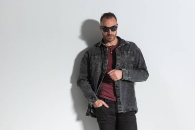 Gri arka planda gri kot ceket giymiş, el ele tutuşmuş, yakışıklı, tıraşsız adam.