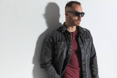 Güneş gözlüklü, kendine güvenen, el ele tutuşan ve stüdyoda gri arkaplanın önüne geçmek isteyen bir adam.