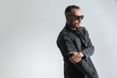 Moda pozisyonunda kolları tutan ve gri arka plana bakan sıradan bir adamın yan görünüşü