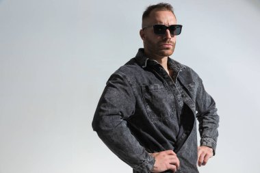 Gri kot ceket giyerken ve gri arka plana bakarken sıradan bir genç adam komik bir poz veriyor. 