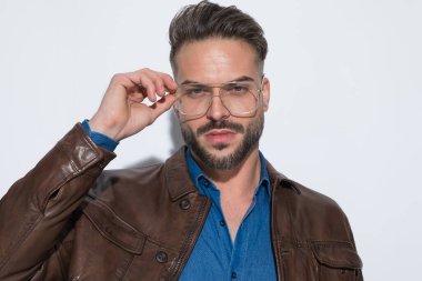 Çekici, sıradan bir adam gözlüğünü takıyor, kameraya bakıyor ve kahverengi deri ceket giyiyor.