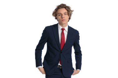 Stüdyoda beyaz arka planda dikilirken elleri ceplerinde poz veren zarif genç bir işadamı.