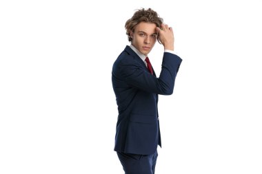 Mavi gözlü, kendine güvenen bir iş adamının portresi. Saç stilini düzenliyor ve düzeltiyor. Stüdyonun beyaz arkaplanının önünden poz veriyor.