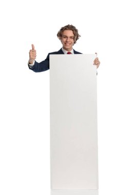Beyaz tahtayı tutan ve gösteren zarif genç işadamı beyaz arka plan önünde baş parmak hareketi yapıyor ve onaylıyor.
