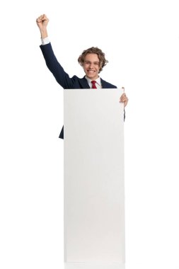 Heyecanlı iş adamı elinde boş tahtayla poz veriyor ve stüdyoda beyaz arkaplan önünde kazananı kutluyor.