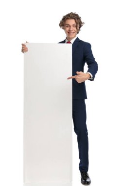 Hevesli genç işadamı beyaz tahta tutuyor, gösteriyor ve sunuyor, işaret ediyor ve gülümsüyor, gururlanıyor ve beyaz arka planda poz veriyor.