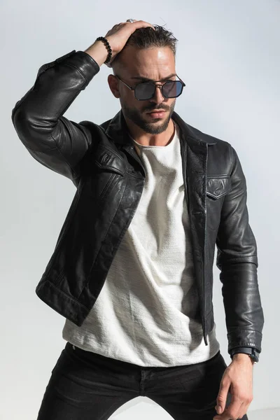 傲慢な男で黒革のジャケット見ながら調整髪型とポーズの前にグレーの背景でスタジオ — ストック写真