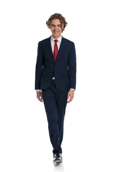 ネイビーブルーのスーツを着てスタジオの白い背景の前を歩く魅力的な若いビジネスマン — ストック写真