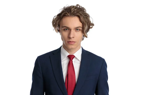 セクシーなブロンドビジネスマンのポートレートともに巻き毛長髪と青い目を身に着けているネイビーブルーのスーツと赤いネクタイとポーズの前に白い背景 — ストック写真