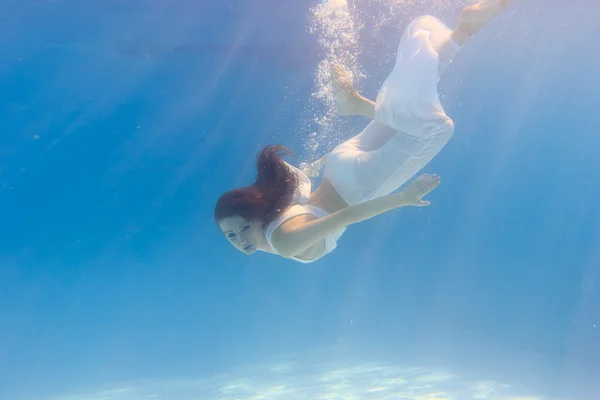 Mujer en un vestido blanco bajo el agua en la piscina — Foto de Stock